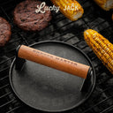 Burger press with wooden handle on a grill with burgers and corn