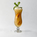 Peachy-colored drink filled with ice and mint leaves on a white background