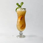 Peachy-colored drink filled with ice and mint leaves on a white background