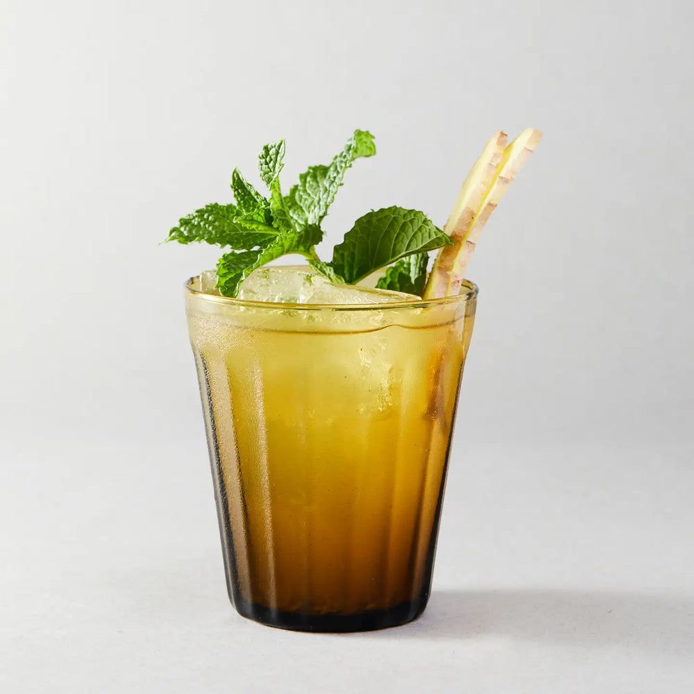 Glass of iced drink with mint leaves and a straw on a light background