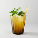 Glass of iced drink with mint leaves and a straw on a light background