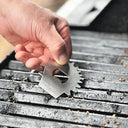 Hand using a grill scraper tool on a grill grate