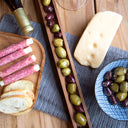 Assorted meats, bread, and a block of cheese and an olive tray on a wooden table.