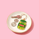 Keychain shaped like a pickle jar on a white dish with coins and keys against a pink background