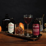 Bittermilk cocktail bottles and glasses on a wooden tray with a dark background