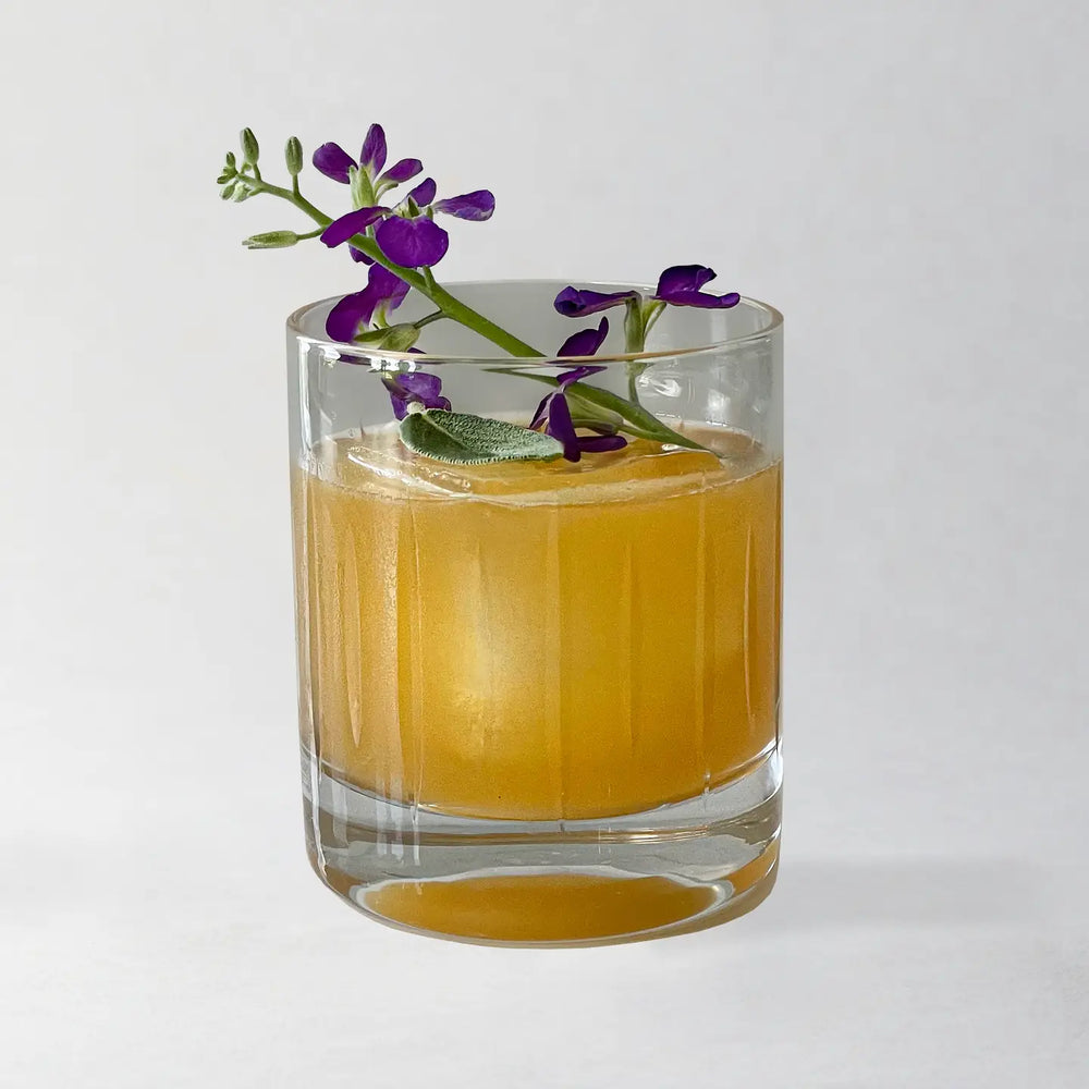 Glass of orange liquid with purple flowers on a white background