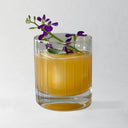 Glass of orange liquid with purple flowers on a white background