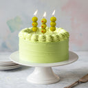 Green cake with olive candles on a white stand against a light background
