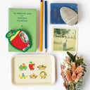Collection of items including a green book, colorful patch, pencil, photo, and decorative Richard Scarry tray on a white surface.