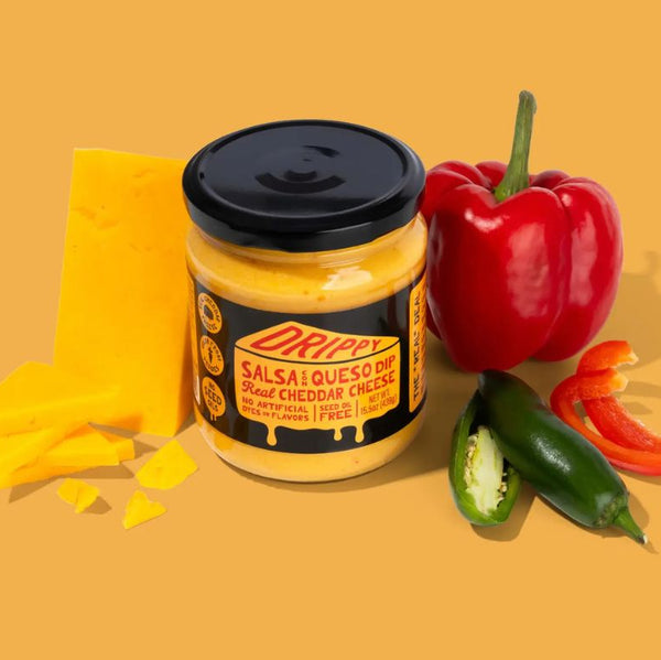 Jar of Drippy Salsa Con Queso surrounded by a block of cheese, red peppers, and jalapenos on a yellow background.
