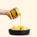 Hand pouring a jar of Drippy's Original Cheese Dip onto tortilla chips in a black bowl.