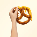 Hand holding a large pretzel with cheese dip on it on a beige background.