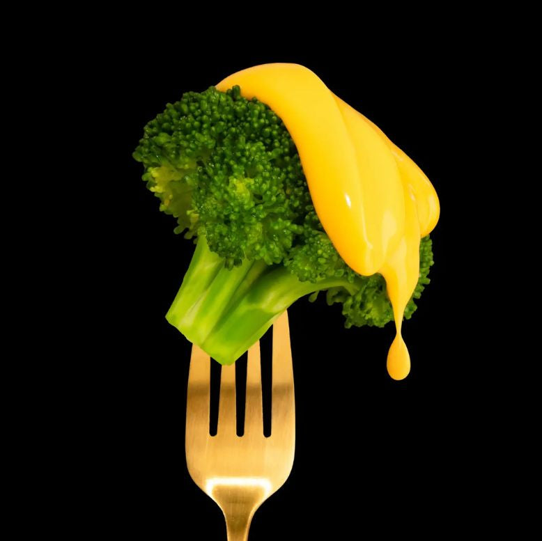 Broccoli on a gold fork with cheese sauce against a black background.