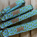 Three different sizes of blue dog collars with a pickle pattern on a wooden surface