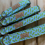Three different sizes of blue dog collars with a pickle pattern on a wooden surface