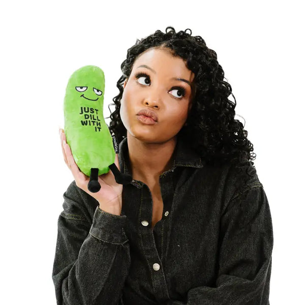 Person holding a green pickle-shaped plushie that says 'Just Dill With It' against a white background