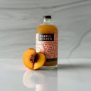 Bottle of Norris Kitchen chamomile peach drink with a peach on a gray marble background