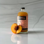 Bottle of Norris Kitchen chamomile peach drink with a peach on a gray marble background