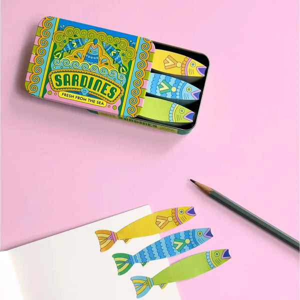 Sardine sticky notes in a colorful tin, a pencil, and paper, on a pink background