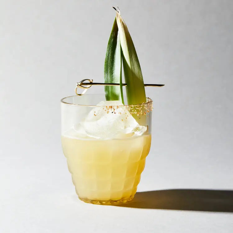 Cocktail with pineapple leaf garnish on a light background