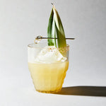 Cocktail with pineapple leaf garnish on a light background