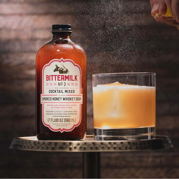 Bittermilk cocktail mixer bottle next to glass filled with orange liquid.